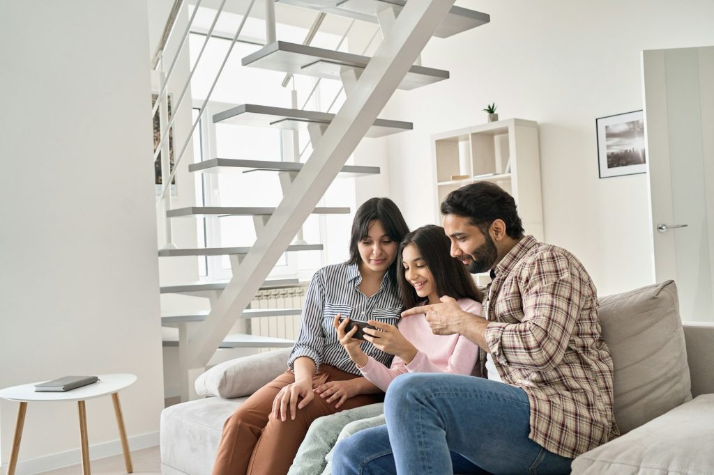 Happy indian family with teen daughter using phone together at home.